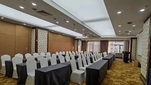 A conference room with rows of white chairs and black tables, a podium, and a carpeted floor. - Sun Moon Lake Hotel (Dalian)