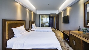 A hotel room with two beds, a television, a desk with a plant, and a bathroom visible through a glass door. - Sun Moon Lake Hotel (Dalian)