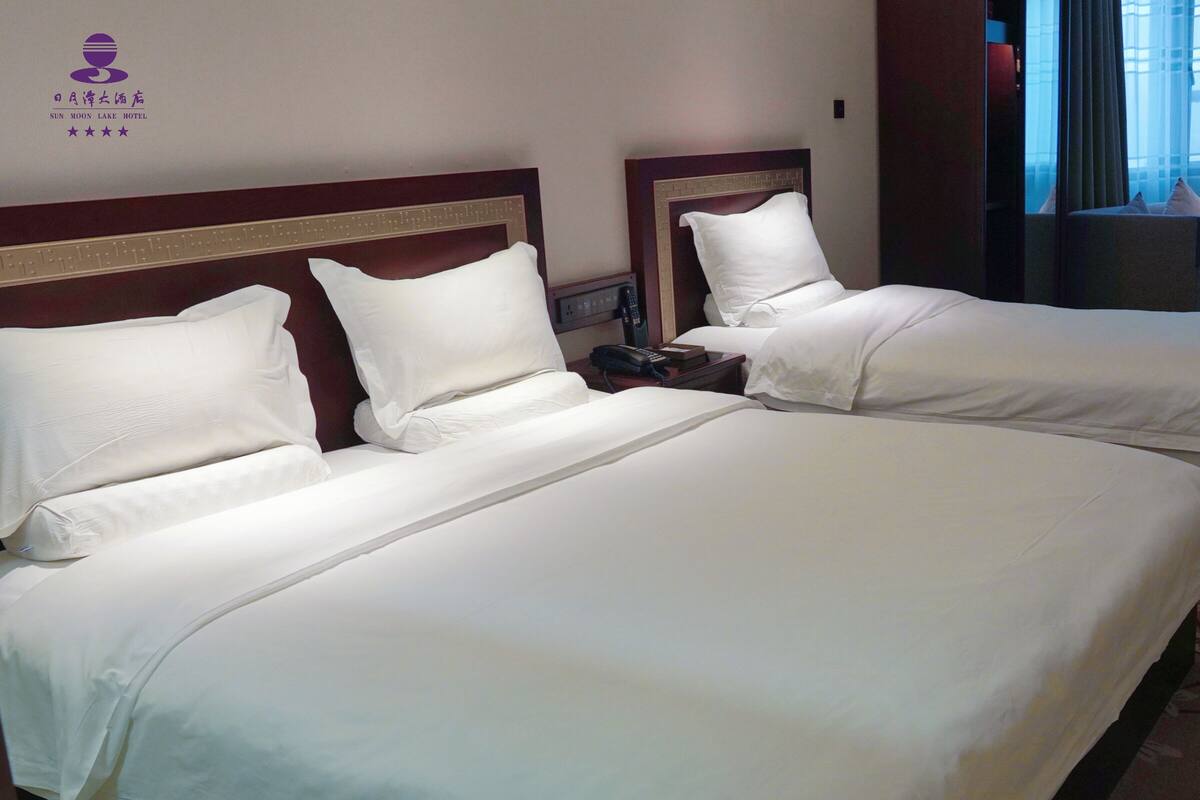Habitación de hotel con dos camas, una mesita de noche con teléfono y un área de descanso con una silla y una mesa.