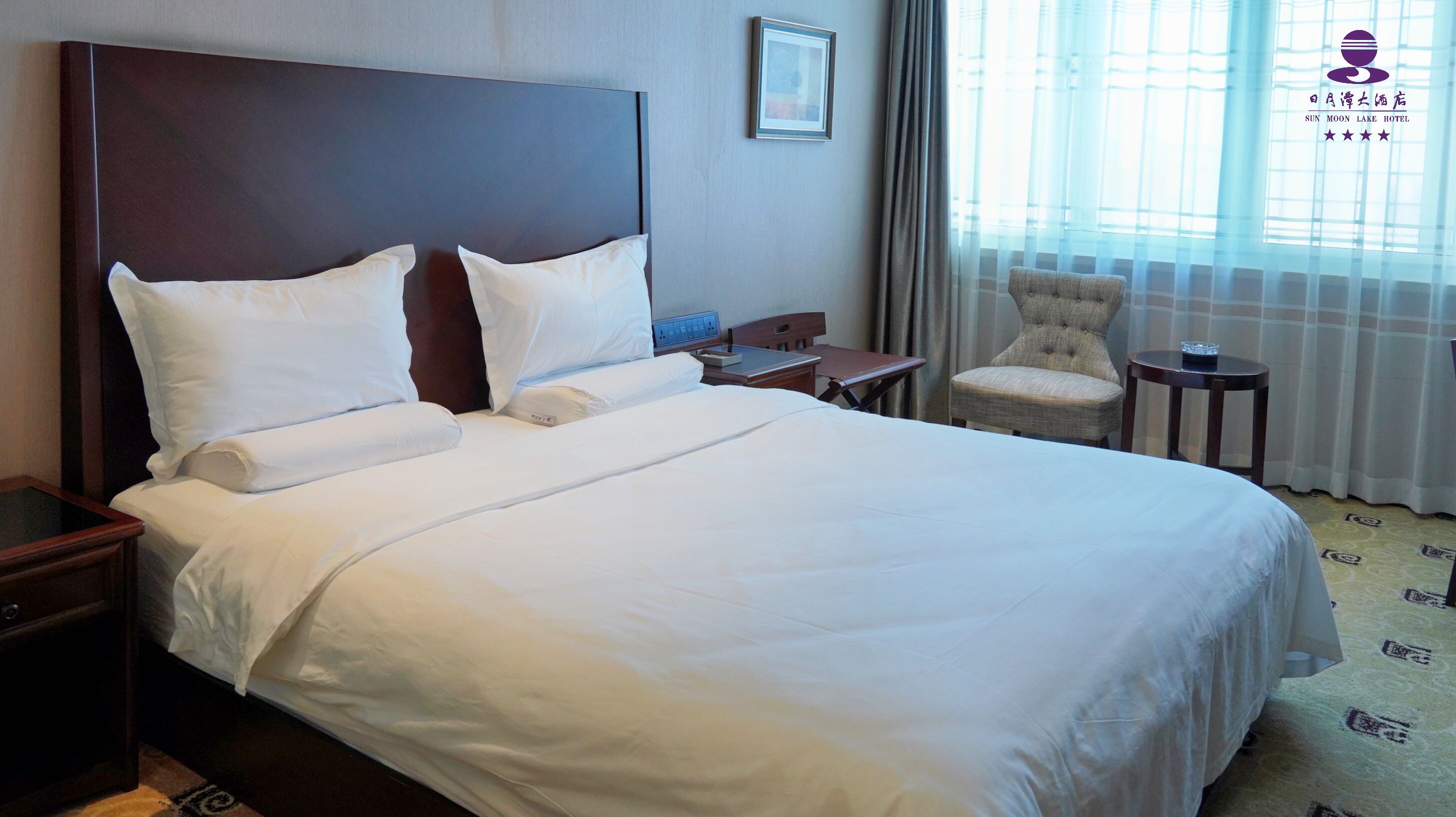 A hotel room with a large bed, a bedside table, a chair, and a window with curtains.