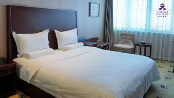 A hotel room with a large bed, a bedside table, a chair, and a window with curtains.