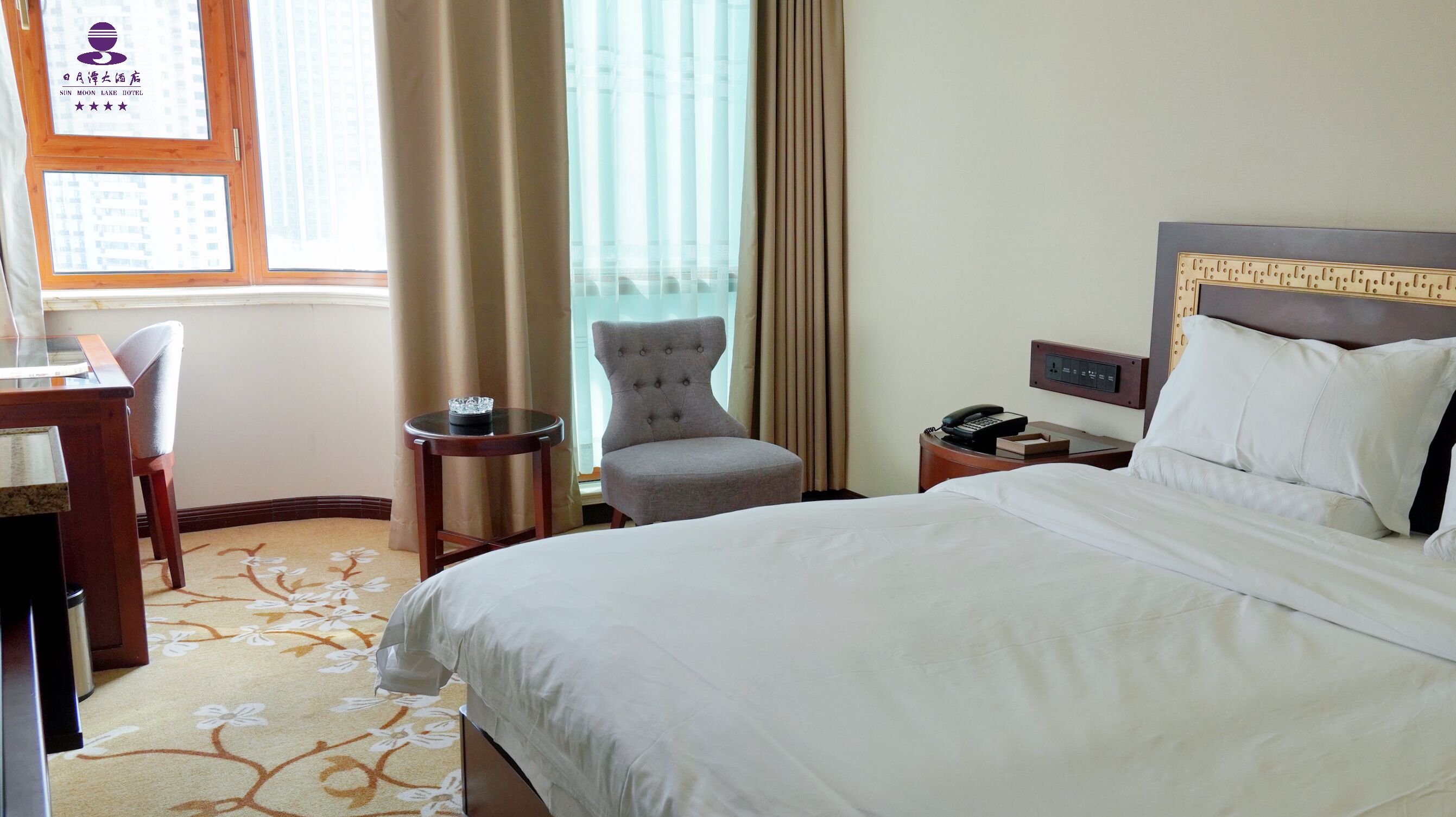 A hotel room with a bed, a chair, a desk, a nightstand, and a window with curtains.