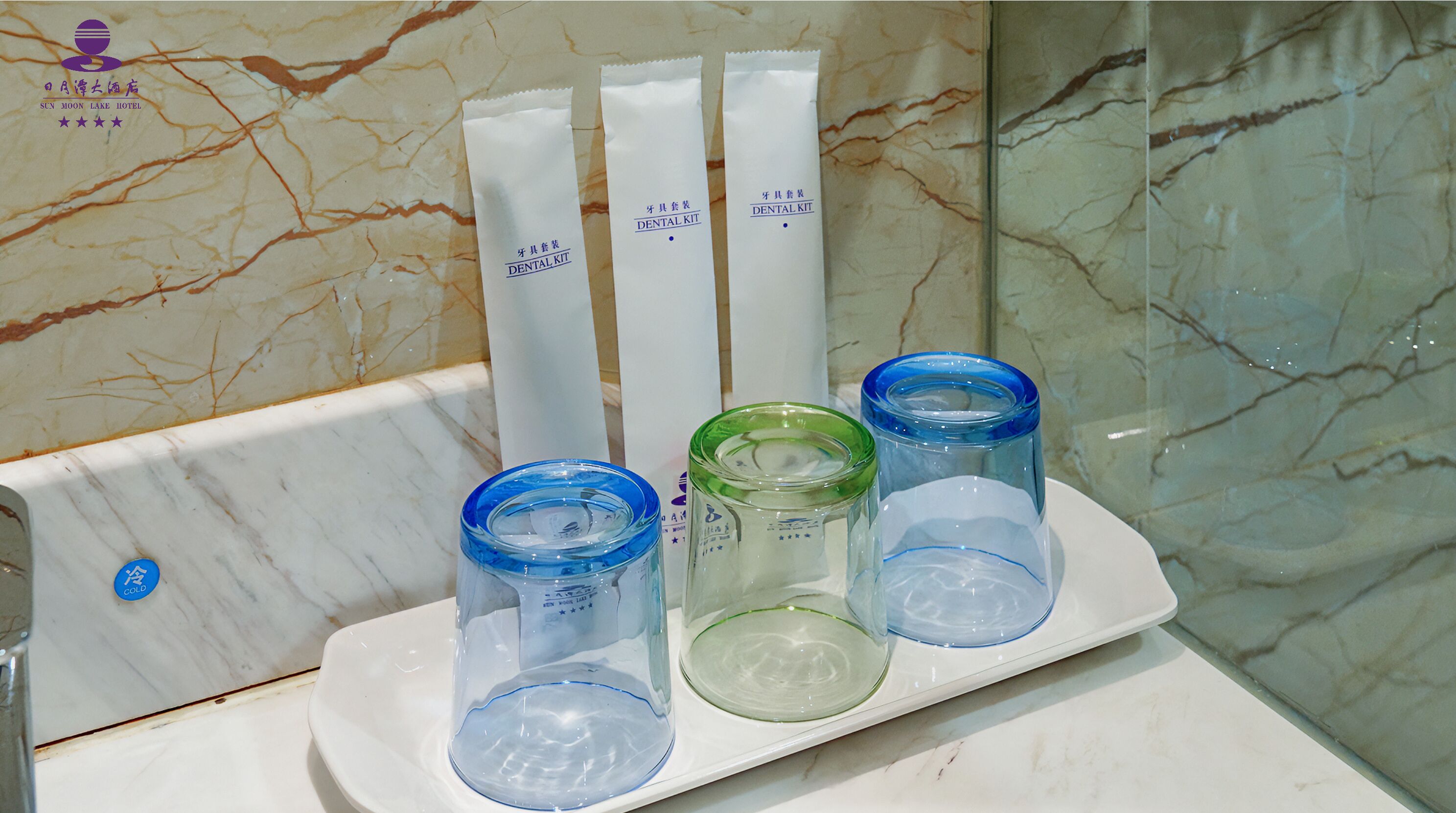 A bathroom sink with a marble countertop and a white wall. There are three dental kits and three glass containers on the sink.