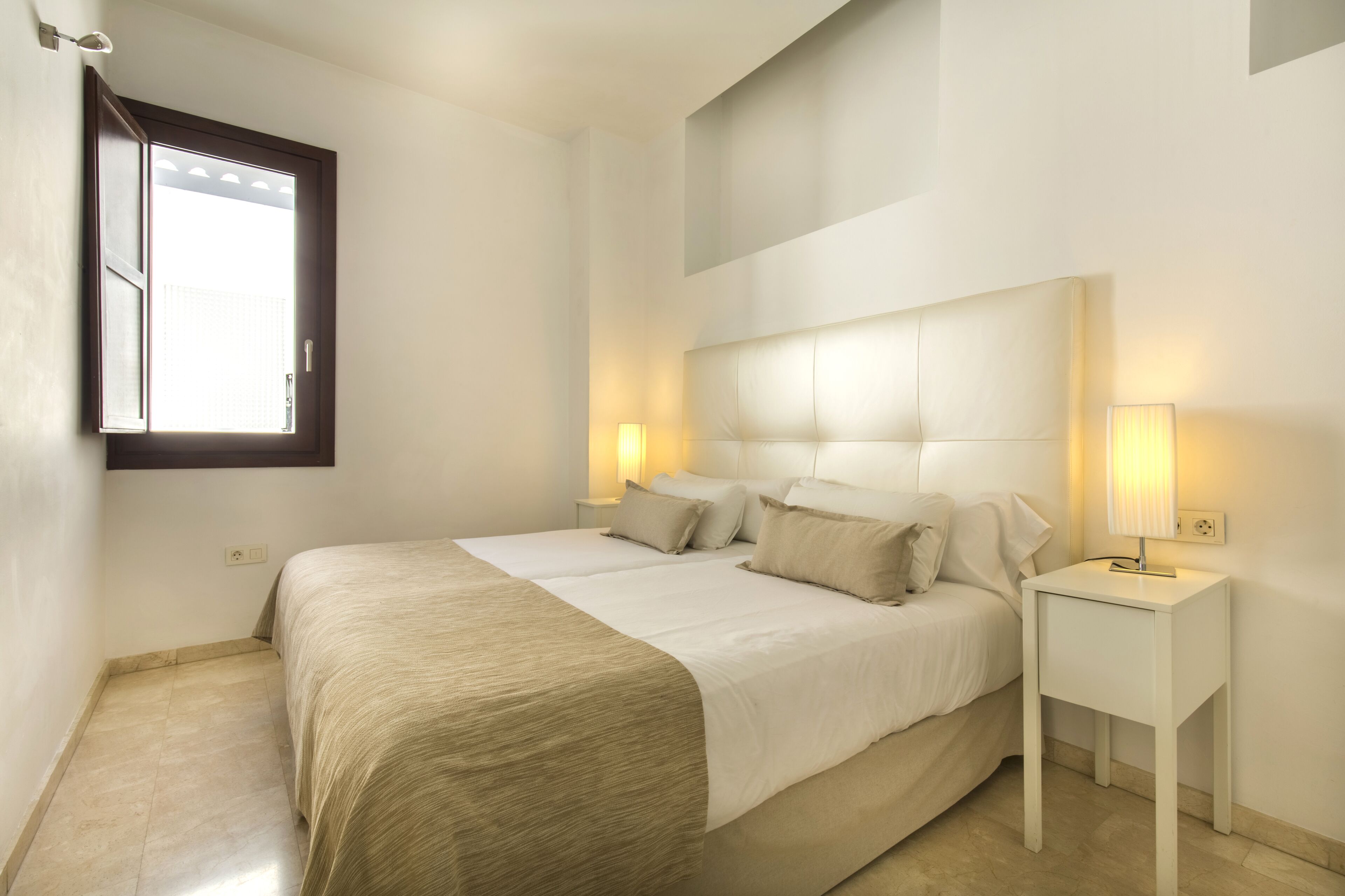 Un dormitorio con cama, lámparas de noche y ventana.