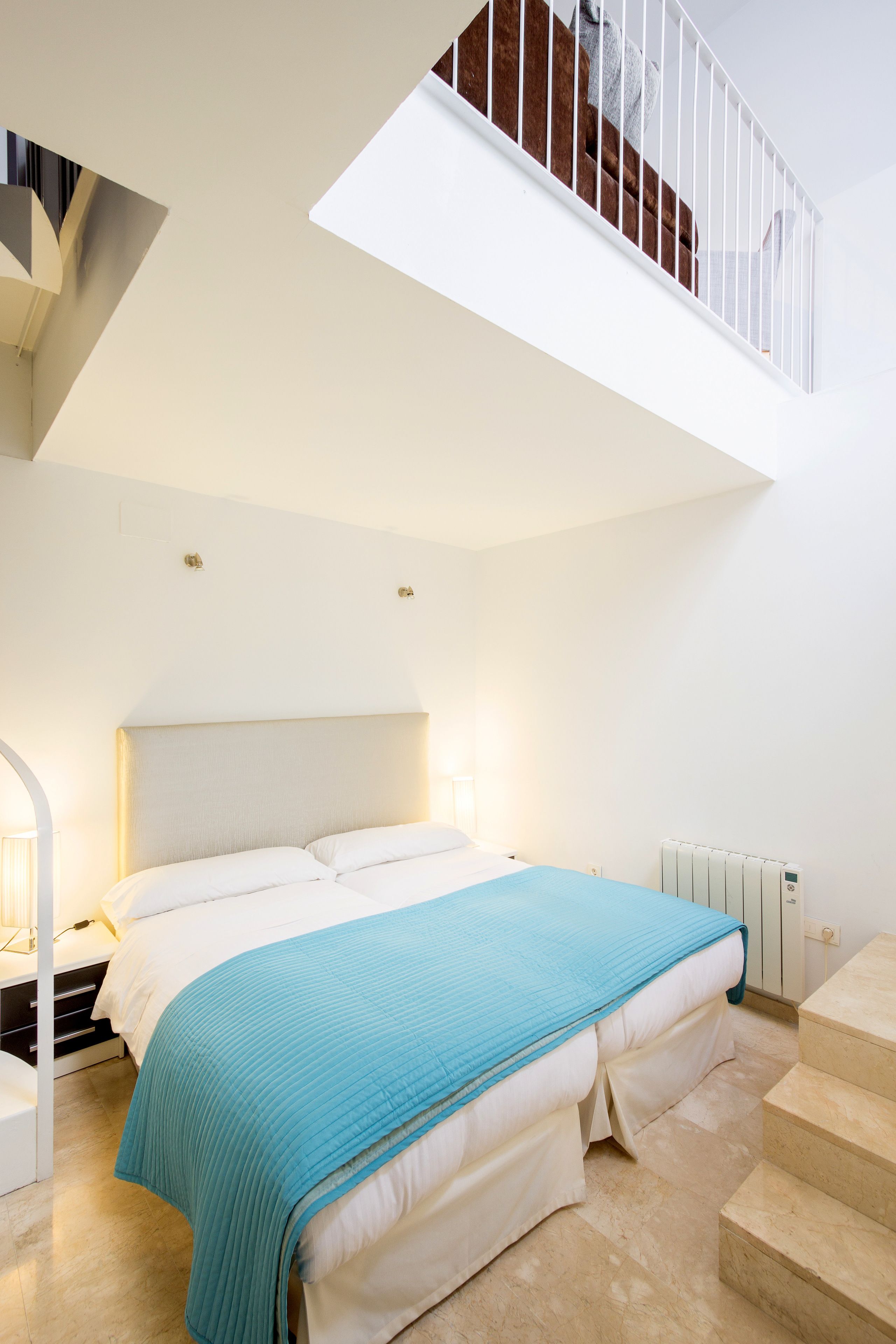 Een slaapkamer met een bed, een nachtkastje, een lamp, een radiator en een trap.
