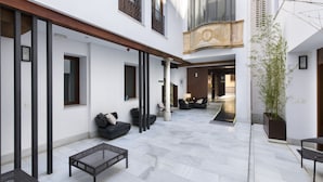 A spacious courtyard with a modern design, featuring a seating area with sofas and a coffee table, a large potted plant, and a view of the interior through a glass door. - tuAnfitrion Elvira Suites (Granada)