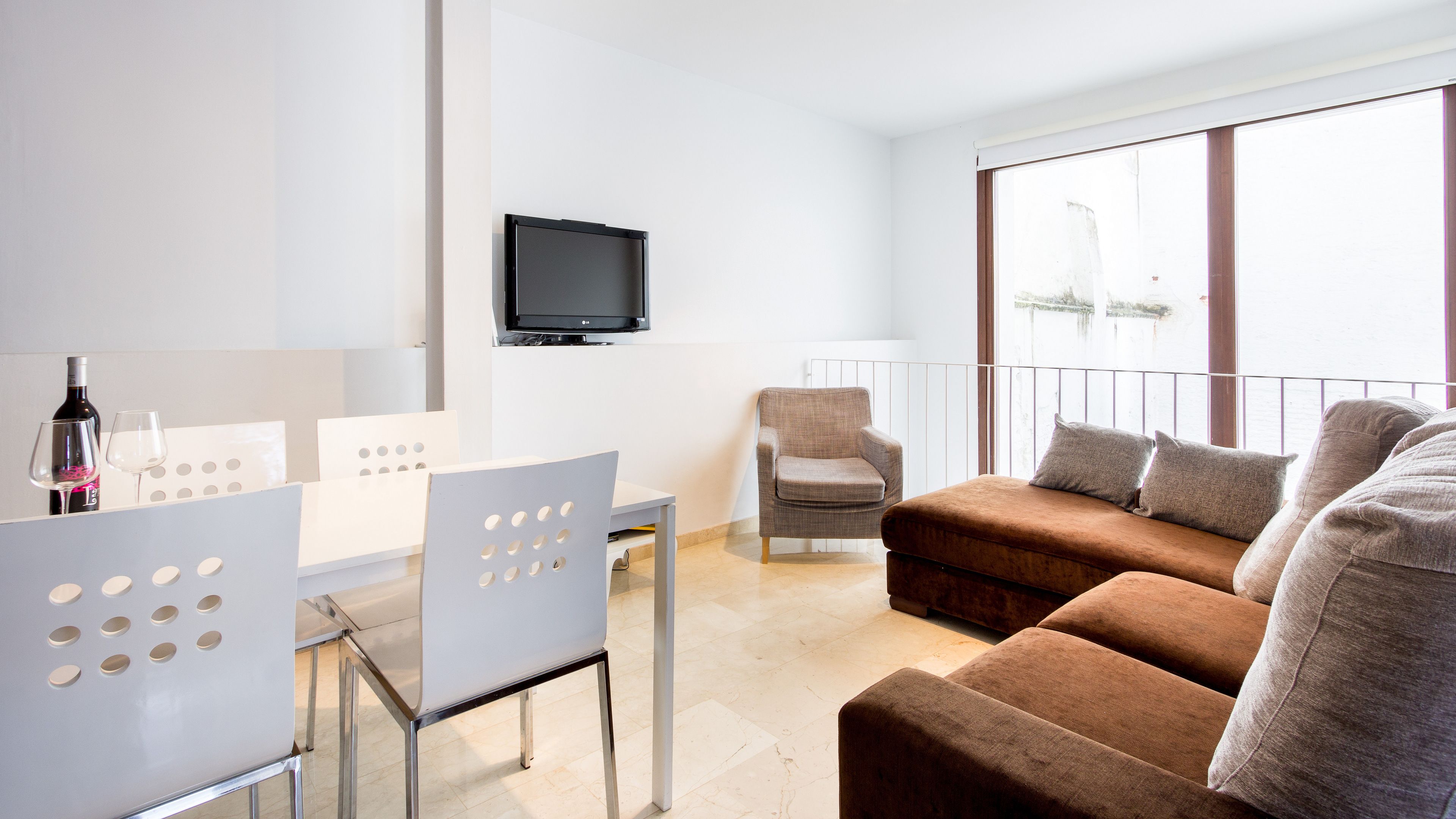 Un salon moderne avec un canapé, un téléviseur fixé au mur et un coin repas comprenant une table et des chaises.