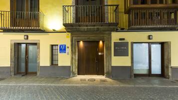 A building with a wooden entrance door, a sign for 'ELVIRA Suites', and a blue 'AT' sign on the left.