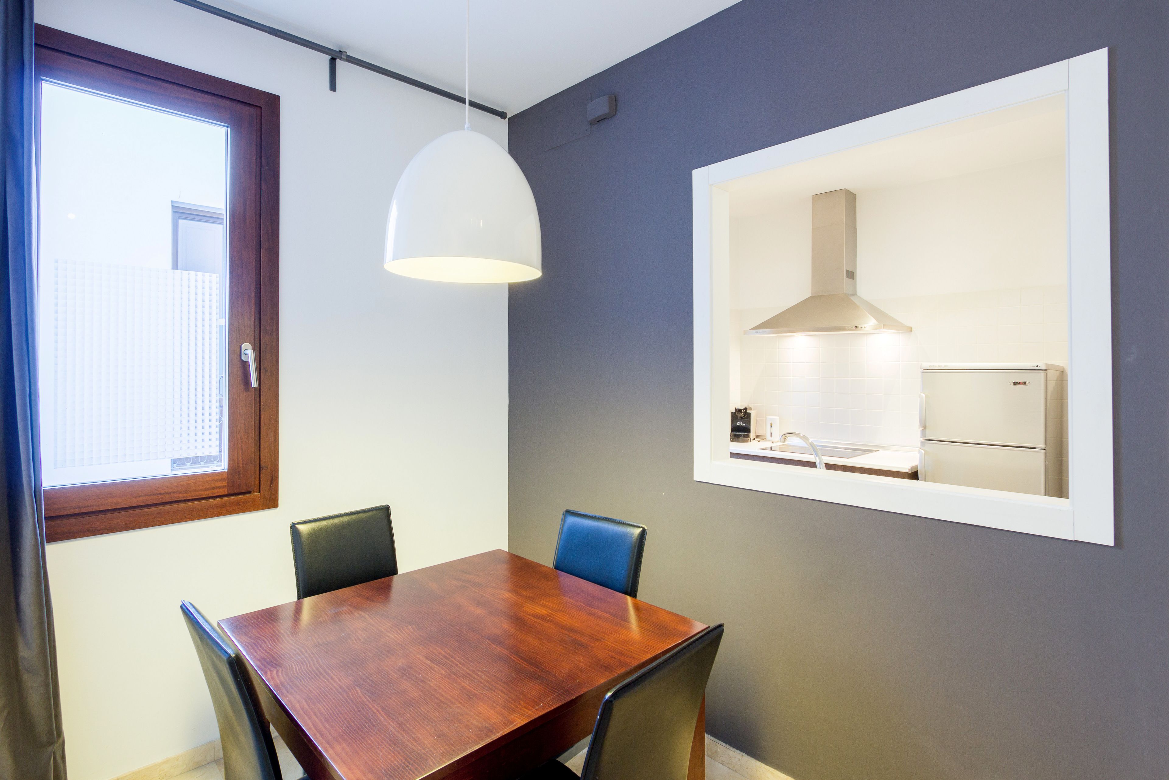 A dining area with a wooden table and four chairs, a pendant light, and a framed picture of a kitchen.