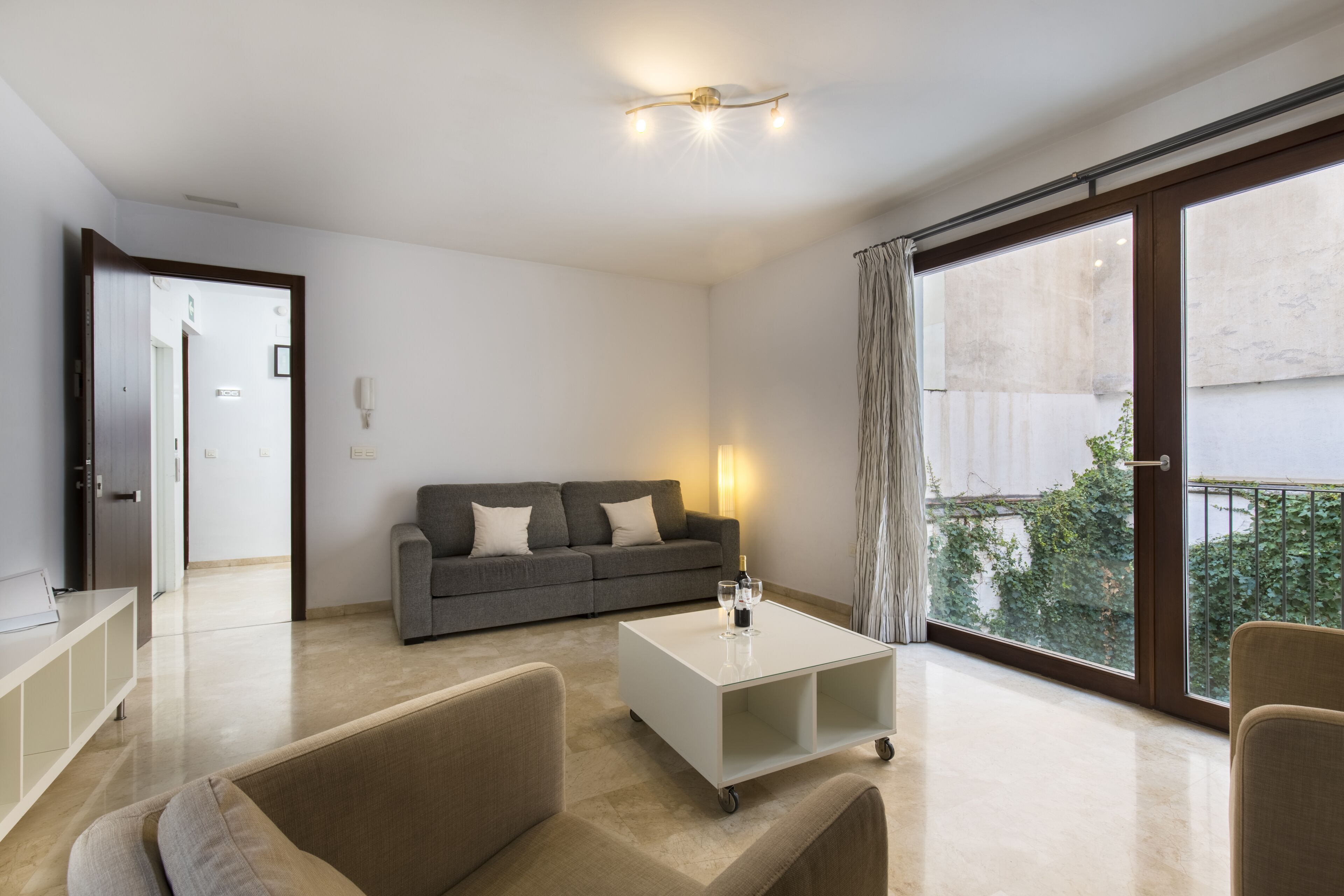 A modern living room with a sofa, a coffee table, and a large window with a view of greenery.