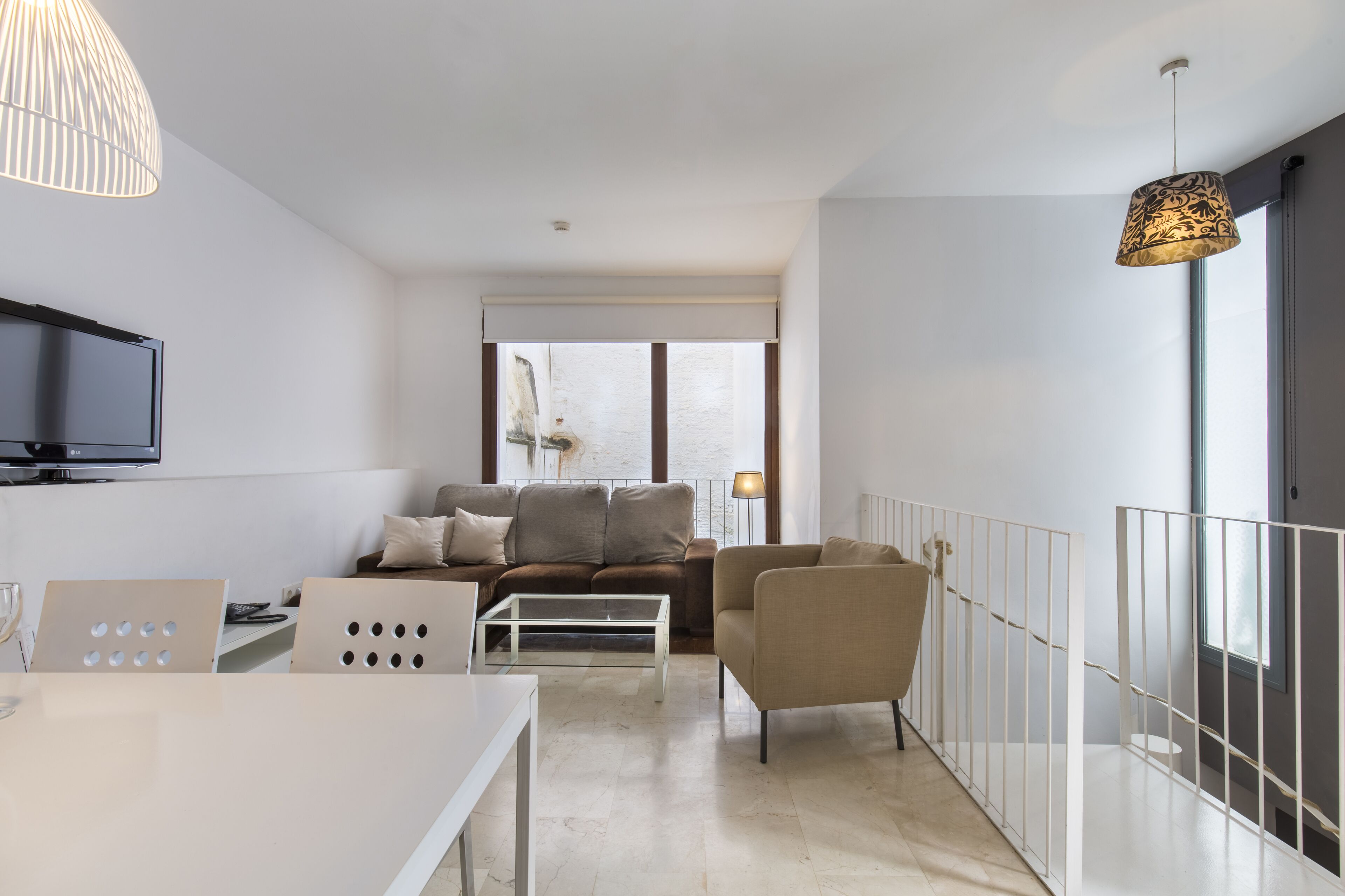 Un soggiorno moderno con divano, tavolino e TV, un balcone con ringhiera e un'ampia finestra.