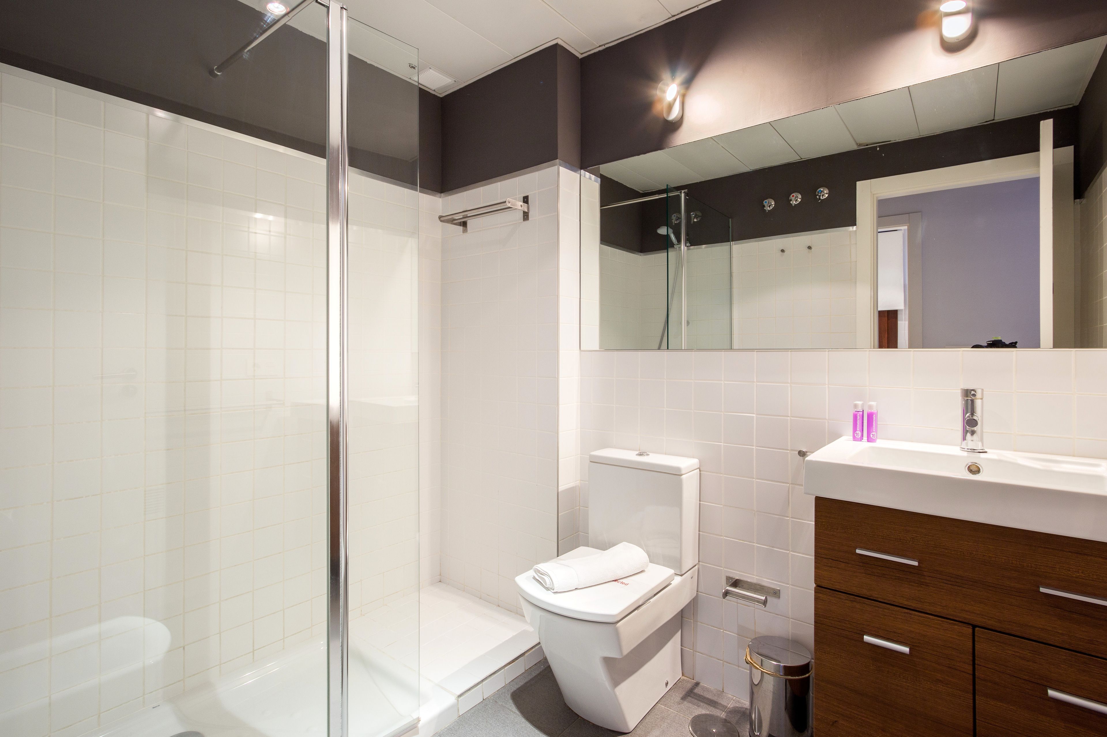 A modern bathroom with a glass shower enclosure, a white toilet, and a vanity with a mirror and cabinet.