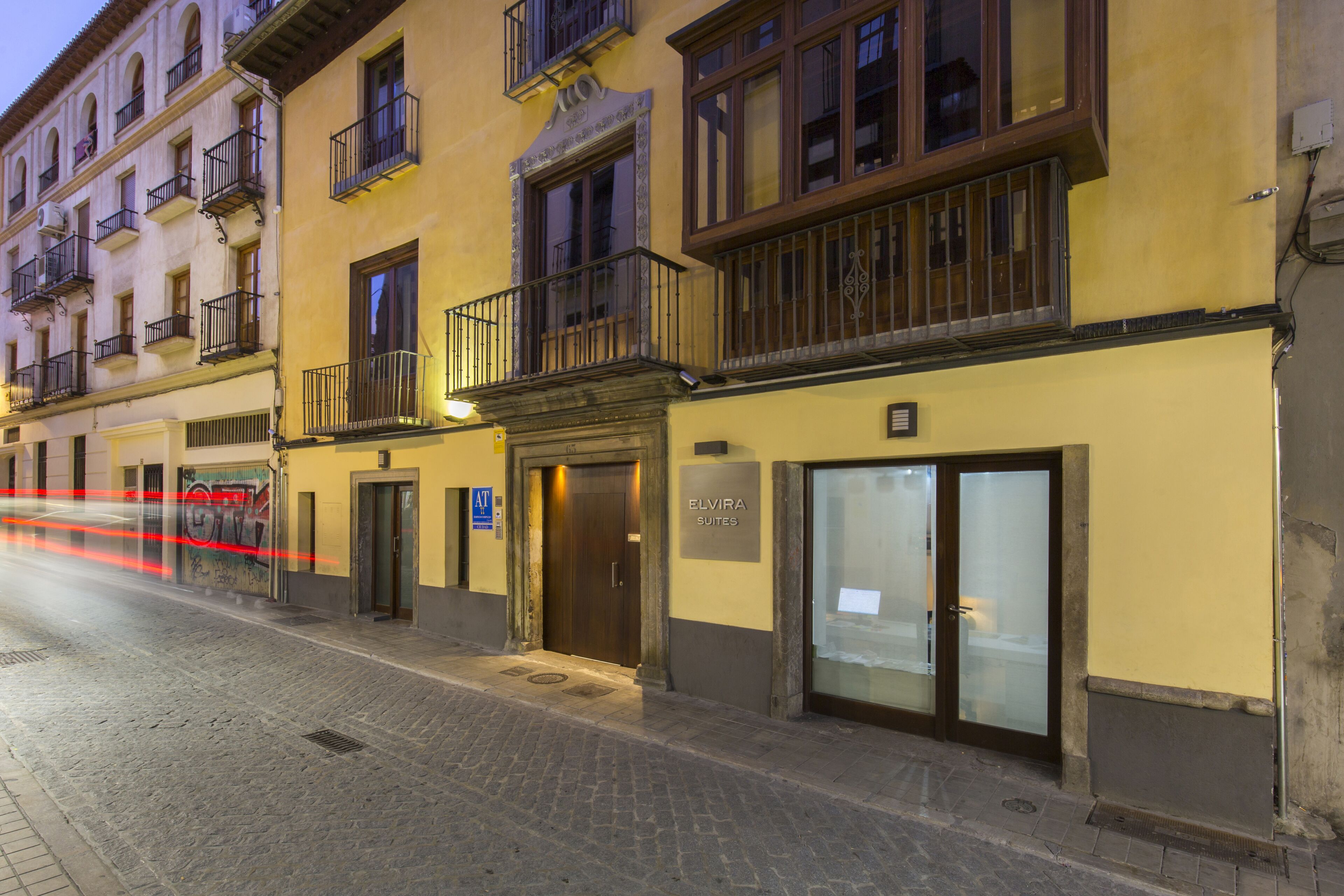 Un edificio con entrada a nivel de calle, un cartel que dice 'ELVIRA SUITES' y una escalera de incendios a la izquierda.
