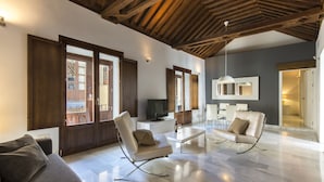 A spacious living room with a high ceiling, a television, a sofa, a coffee table, and a dining area. - tuAnfitrion Elvira Suites (Granada)