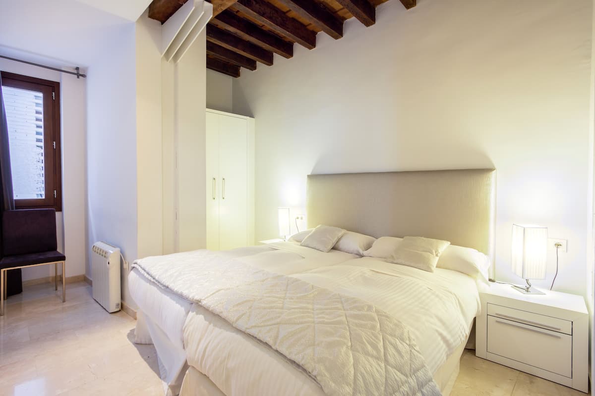 A bedroom with a bed, bedside table, lamp, and a radiator.