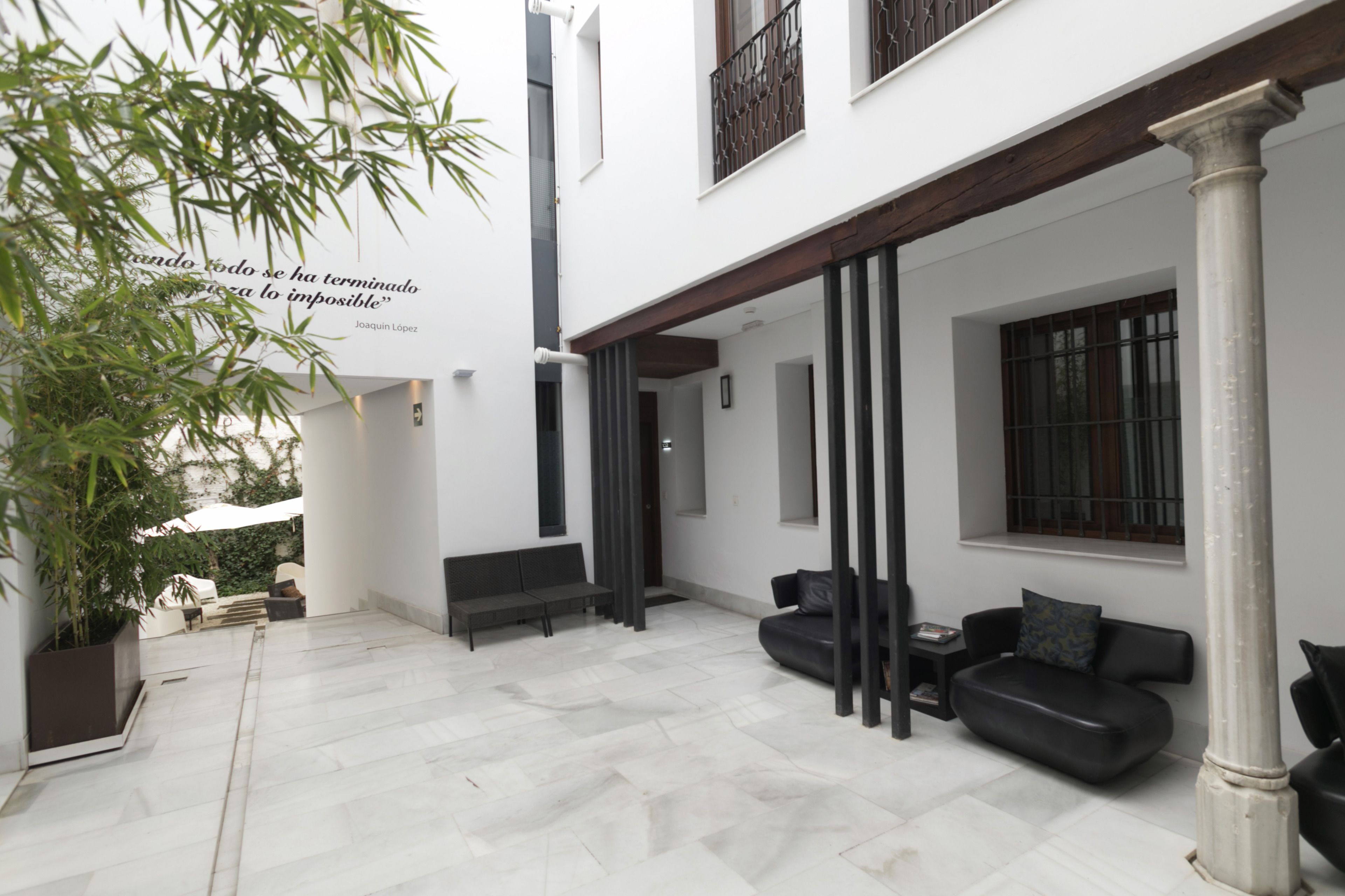 Un patio exterior moderno con suelo de baldosas blancas, sofás negros y una planta en maceta.