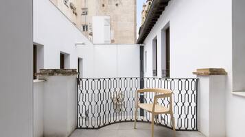 Un patio estrecho con una silla de madera, paredes blancas y una verja decorativa de metal.