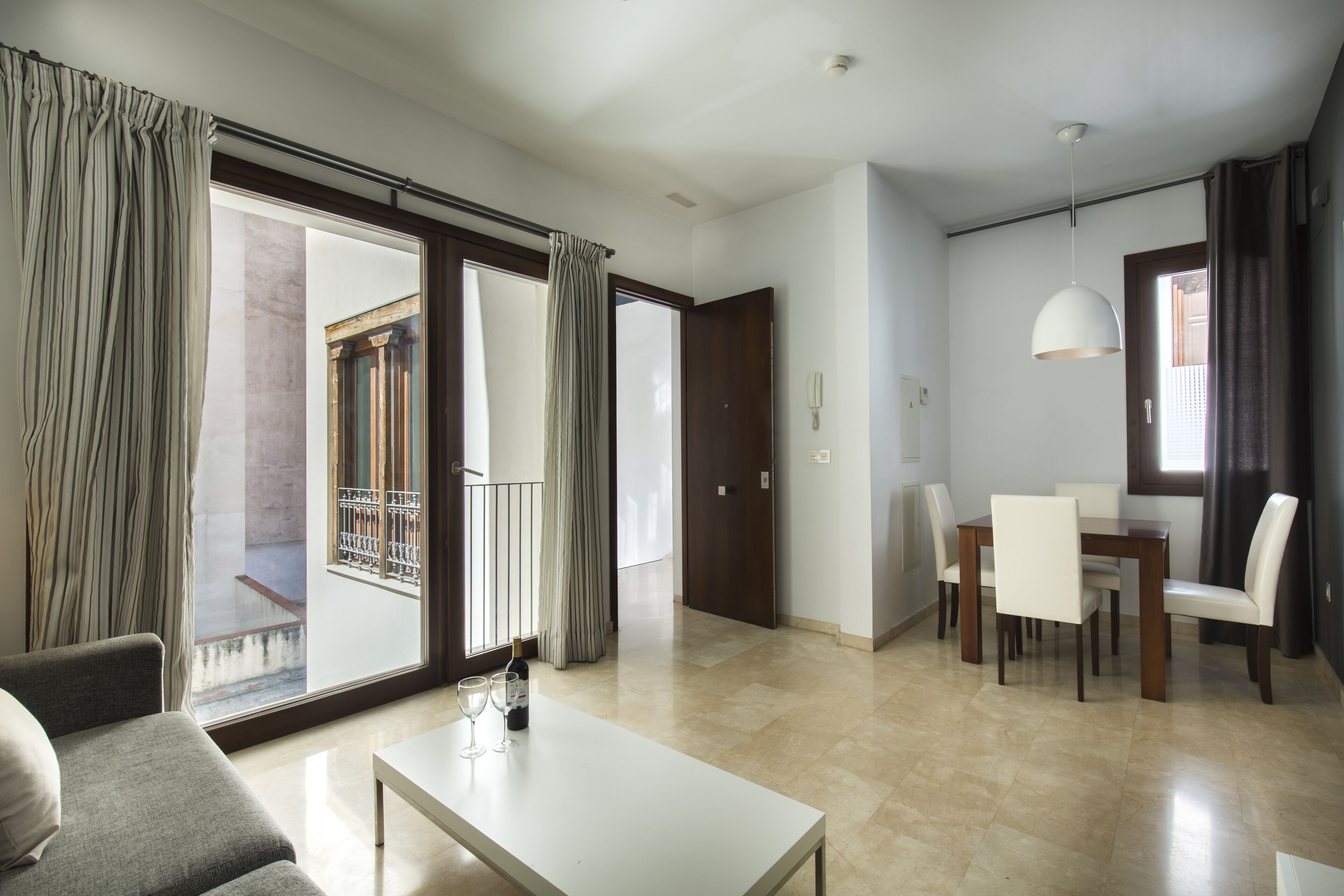 Ein geräumiges Wohnzimmer mit Sofa, einem Esstisch mit Stühlen, einem Couchtisch und einem großen Fenster mit Vorhängen.