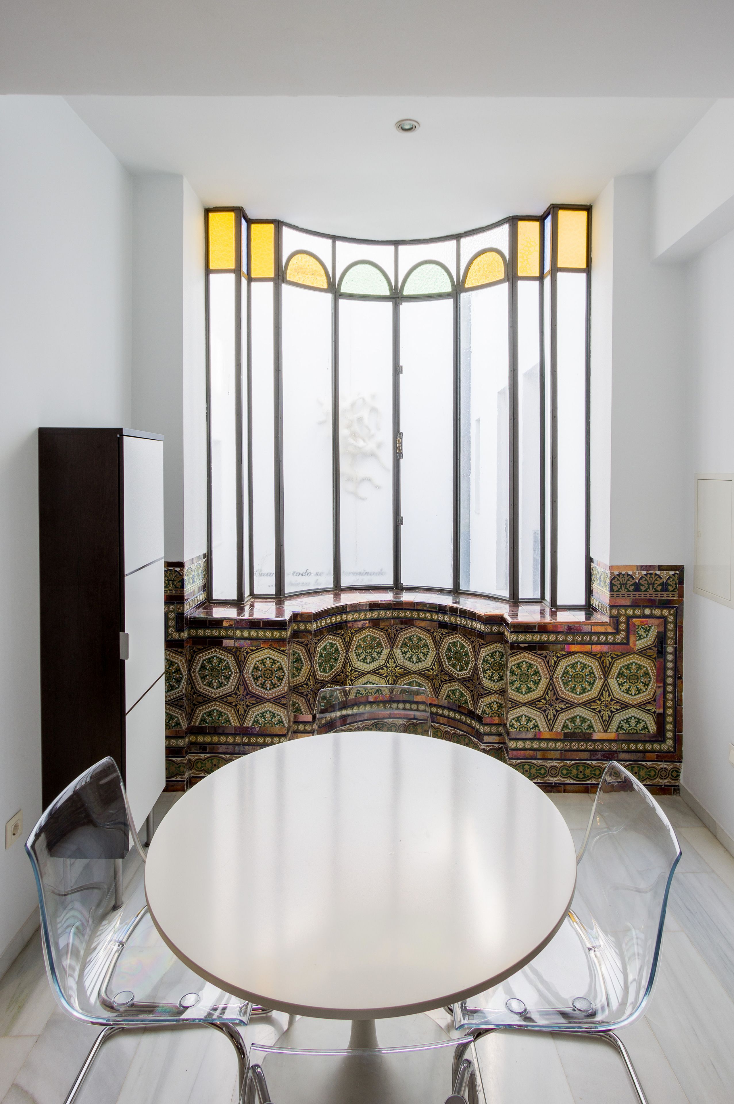 A dining area with a round table, clear chairs, a decorative partition, and a view through a window with a patterned design.