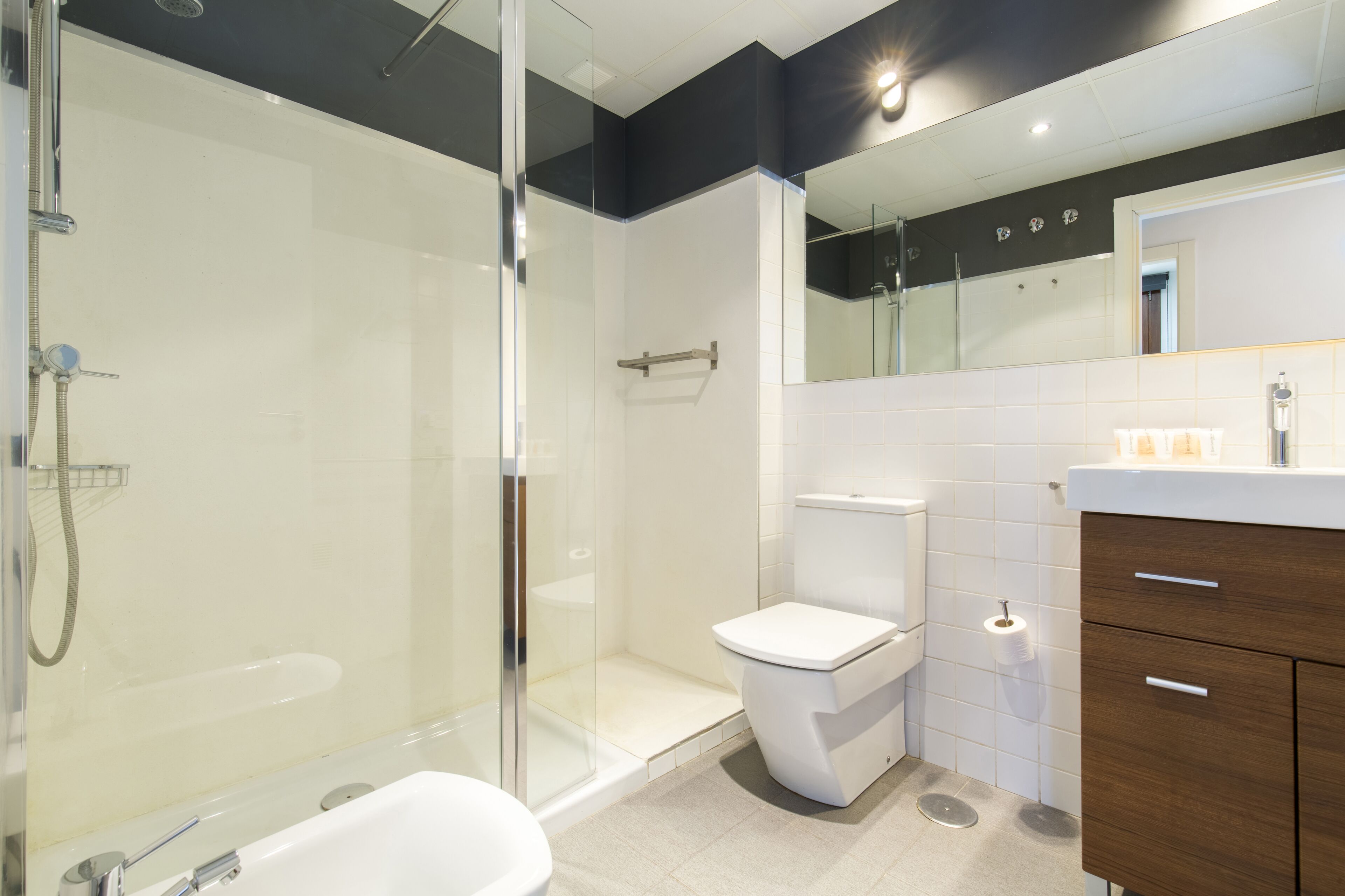 Un baño moderno con ducha de vidrio, inodoro blanco y tocador de madera con espejo.