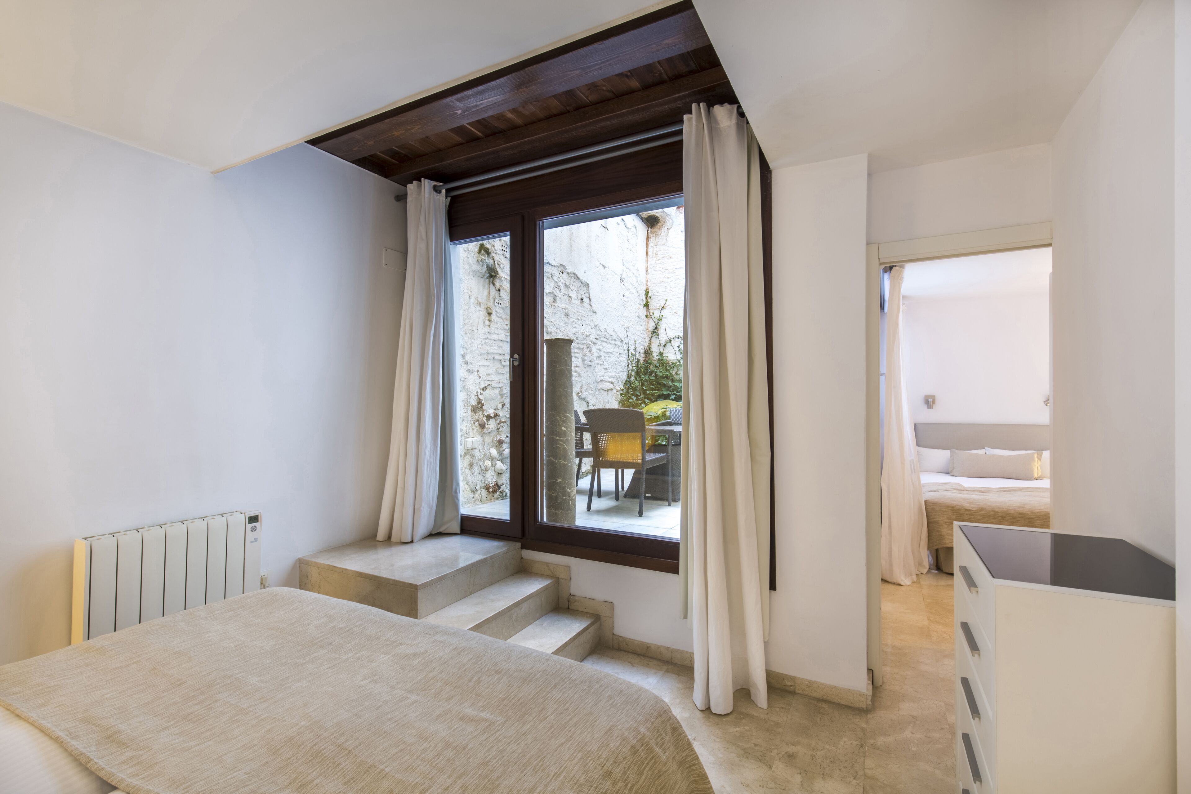 Ein Schlafzimmer mit einem Bett, einem Schreibtisch, einem Heizkörper und einem Fenster mit Vorhängen.