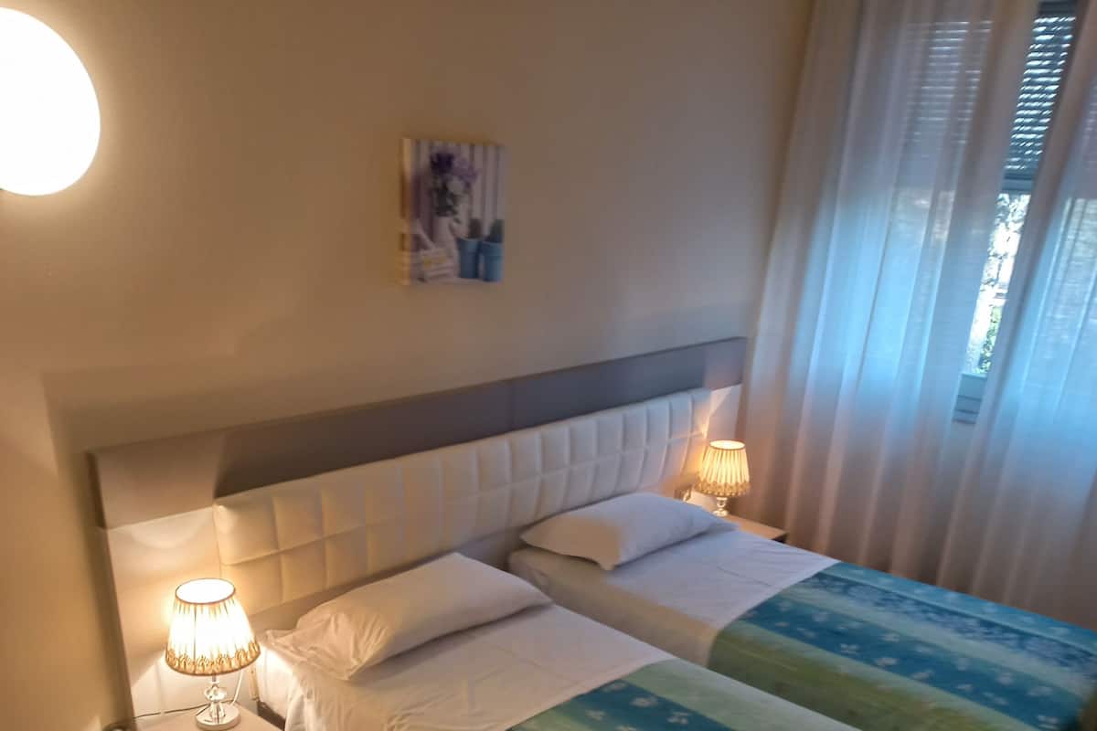 A hotel room with two beds, a nightstand, a lamp, and a chair.