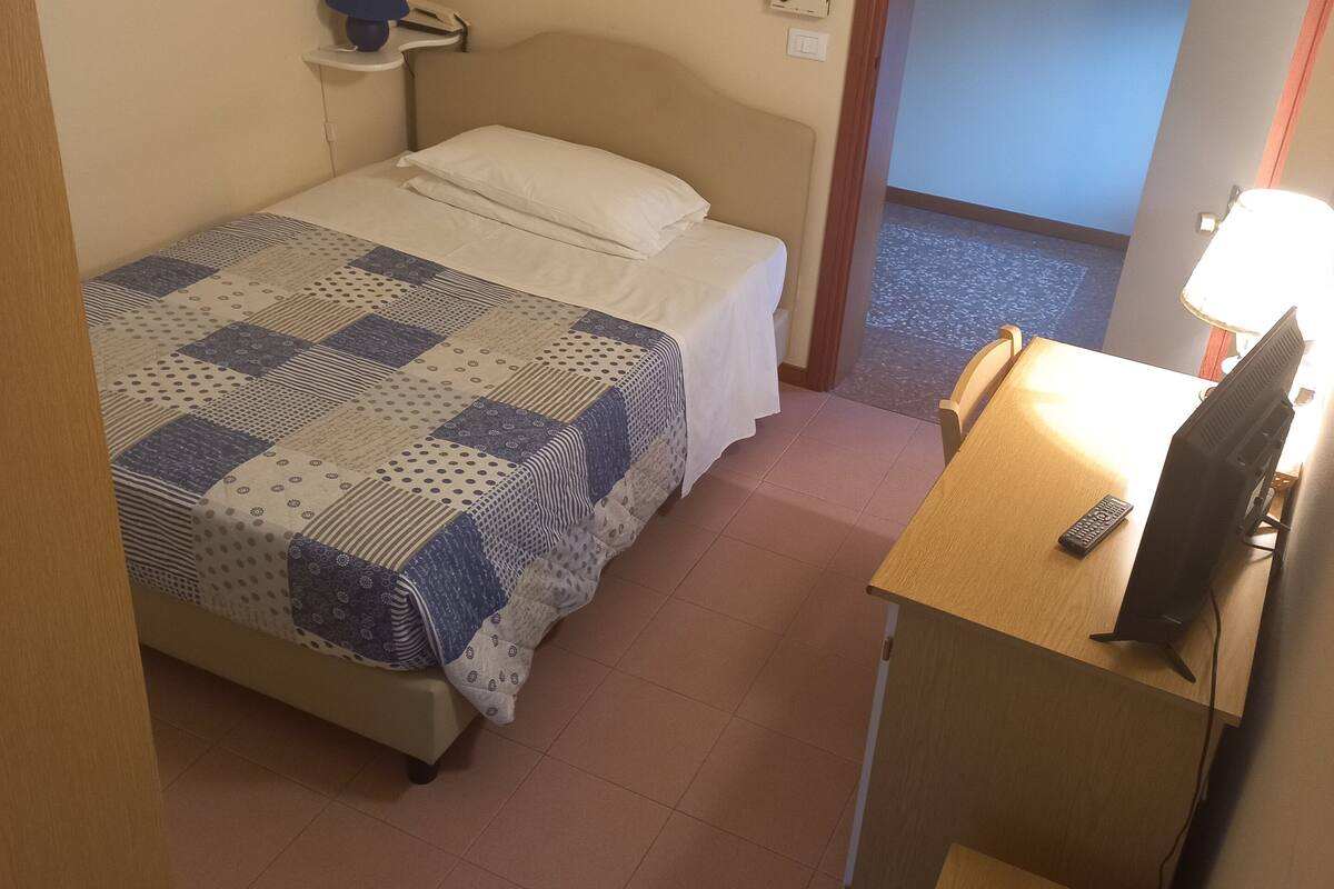 A small, neatly arranged bedroom with a bed, a desk with a computer, and a chair.