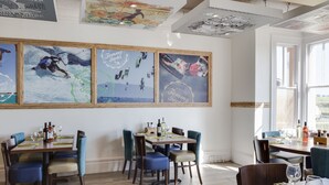 Un comedor con mesas y sillas de madera, carteles enmarcados en la pared y vistas al exterior a través de amplias ventanas.
