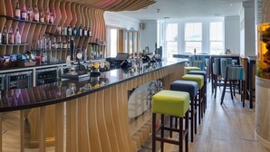 Un área de bar moderna con una barra alargada, taburetes y una amplia variedad de botellas.