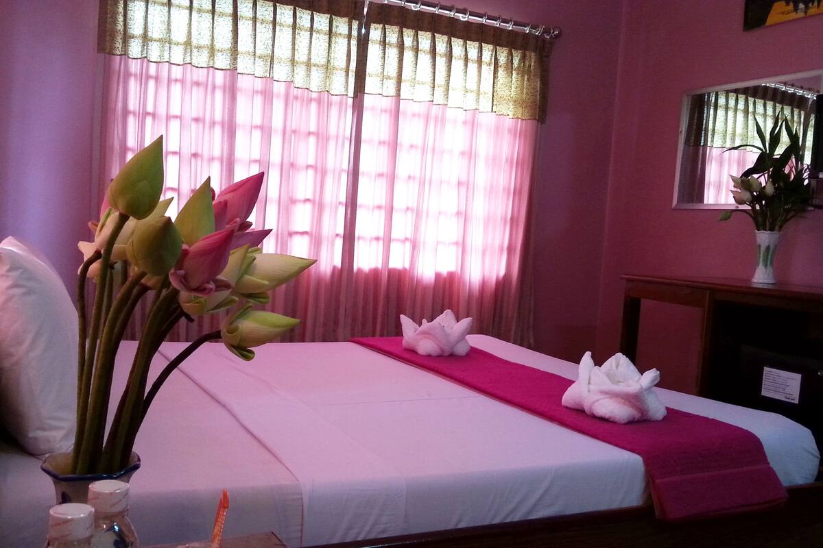 Une chambre d’hôtel avec un lit, un vase de fleurs et une fenêtre avec des rideaux.