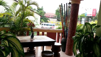 A balcony with a table, chairs, and potted plants. A white van is visible in the background.
