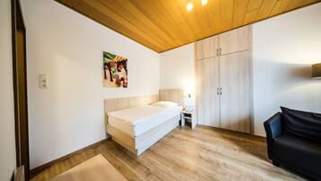 A room with a bed, a wooden ceiling, a wardrobe, a small table with a lamp, and a painting on the wall.
