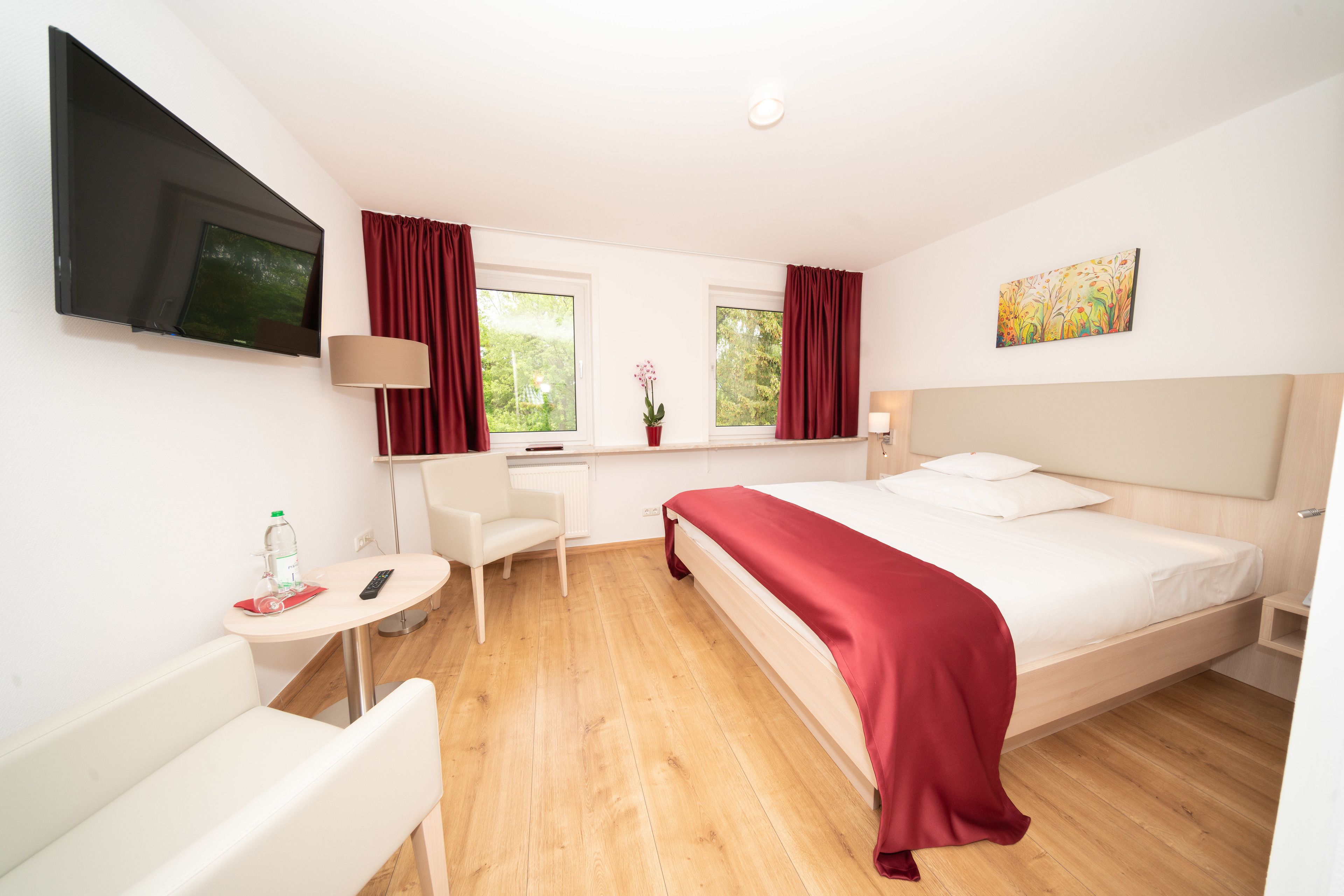Una habitación de hotel con cama, escritorio, silla, televisor y ventanas con cortinas.