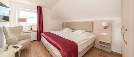 Una habitación de hotel moderna con una cama, un escritorio, una silla, un televisor y un ventanal con cortinas.