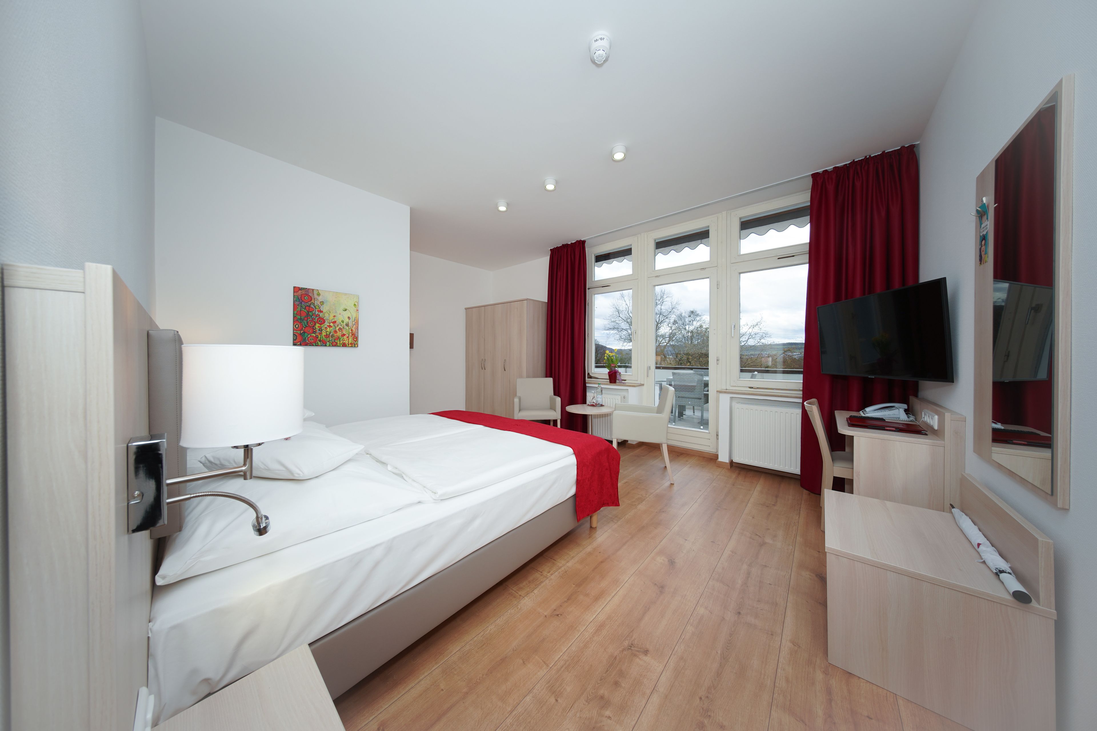 Een hotelkamer met een bed, bureau, stoel, televisie en een raam met gordijnen.