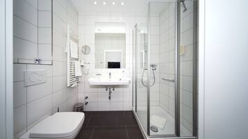 Un baño moderno con inodoro, lavamanos y ducha con mampara de vidrio.