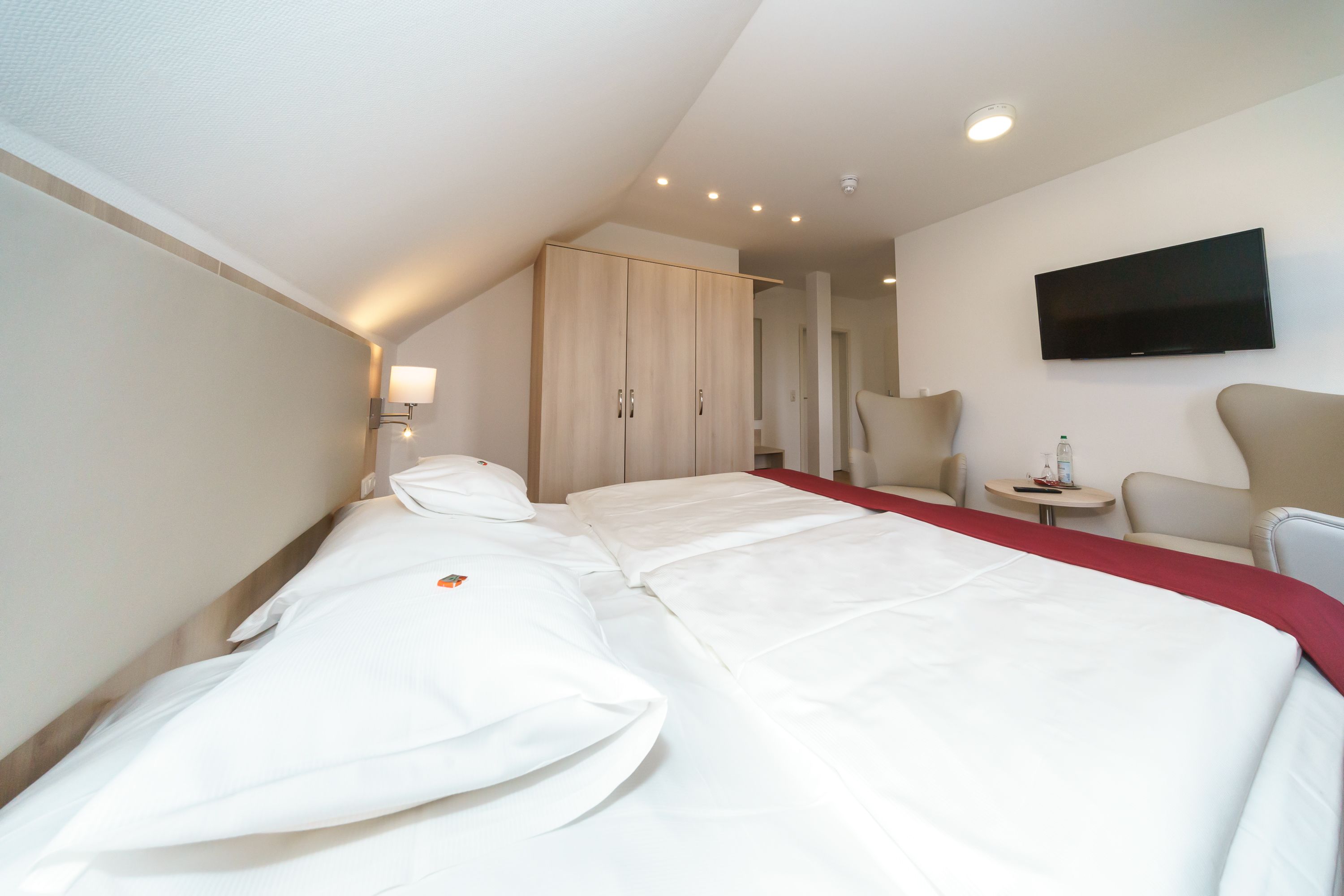 Habitación de hotel con una cama, televisión montada en la pared, una mesita pequeña y una silla.