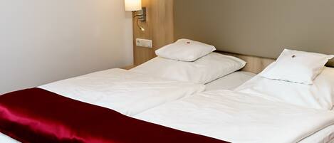 A hotel room with a bed, white bedding, a red throw blanket, and a wall-mounted light fixture.