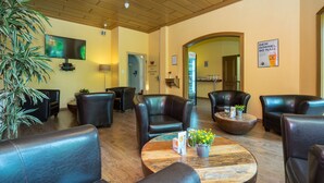 Een hotel lobby met lederen zitplaatsen, een houten bijzettafeltje met bloemen, een flatscreen televisie en een Coca-Cola koelkast.
