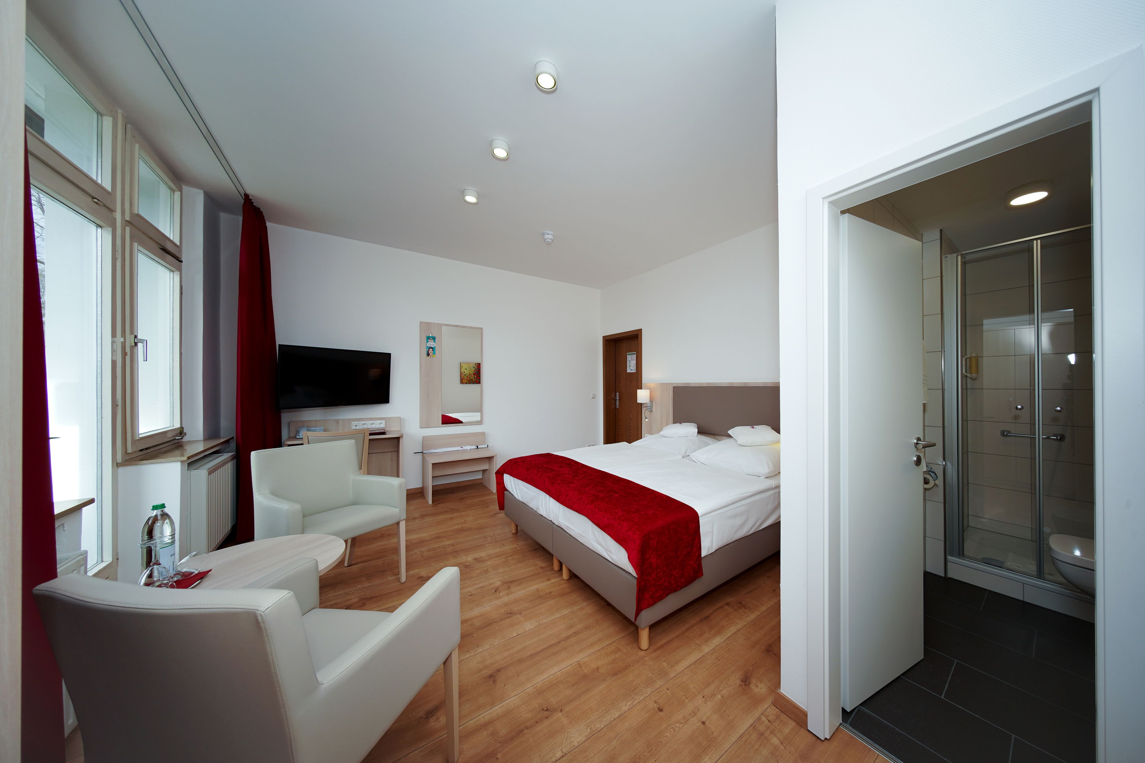 A modern hotel room with a bed, a desk, a chair, a TV, and a shower area.