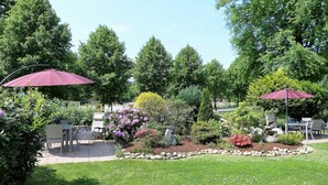 Een terras met buitenmeubilair, een tuin met diverse planten en twee grote parasols die schaduw bieden.