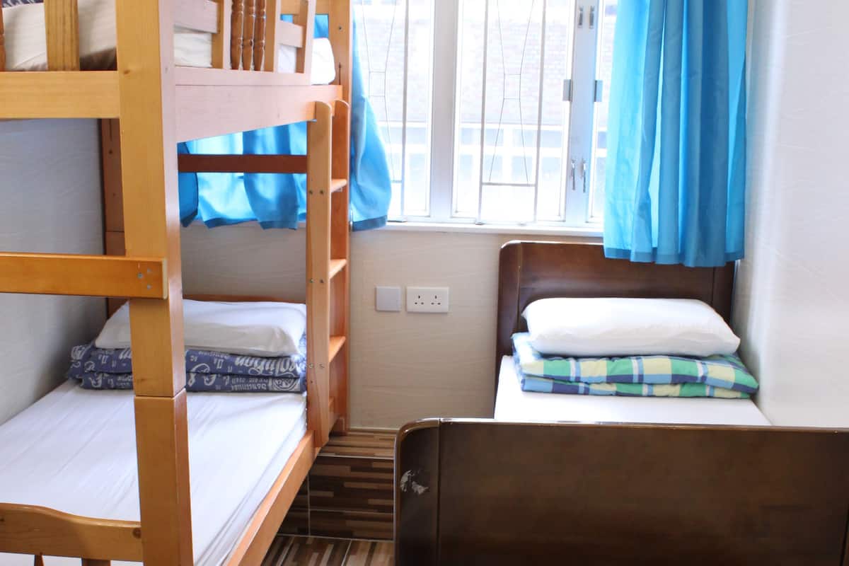 A room with bunk beds, a single bed, and a window with blue curtains.