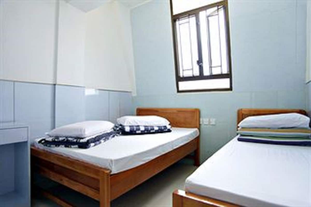 A small, simple room with two wooden beds, white bedding, and a window with bars.