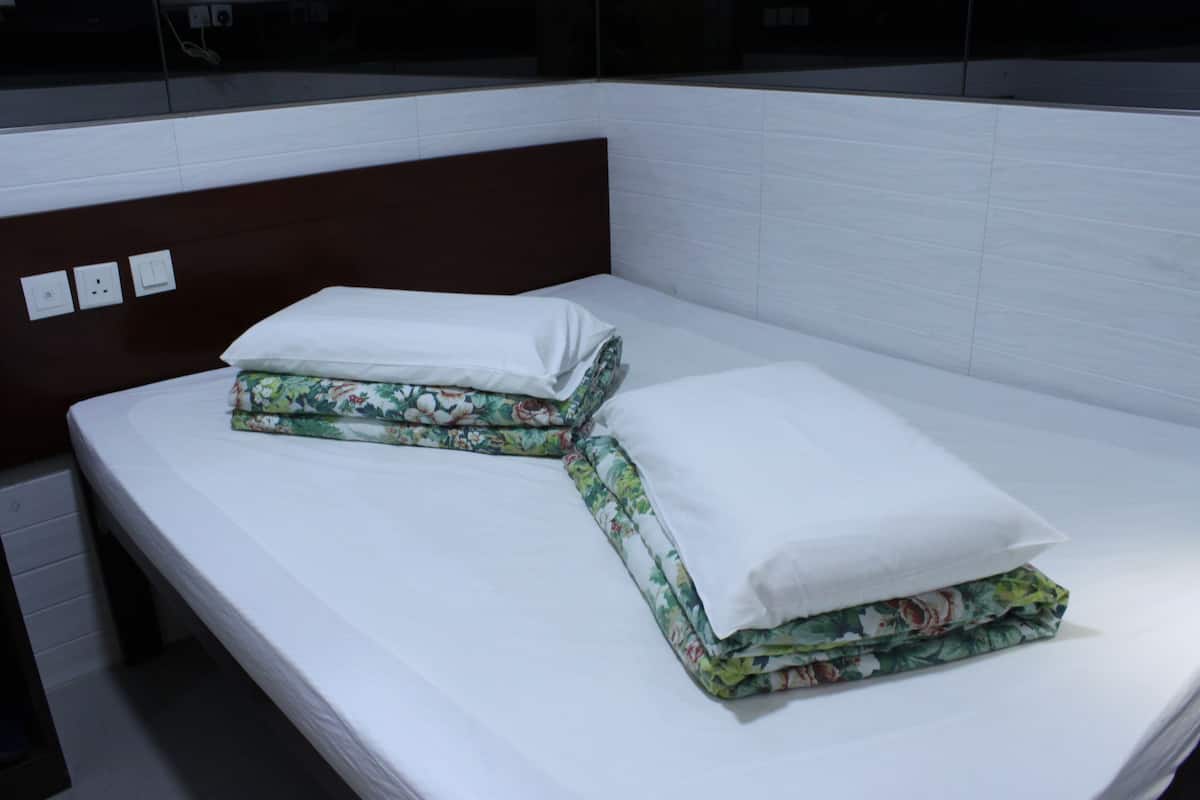 A single bed with white bedding and floral-patterned sheets, a wooden headboard, and a white tiled wall with electrical outlets.