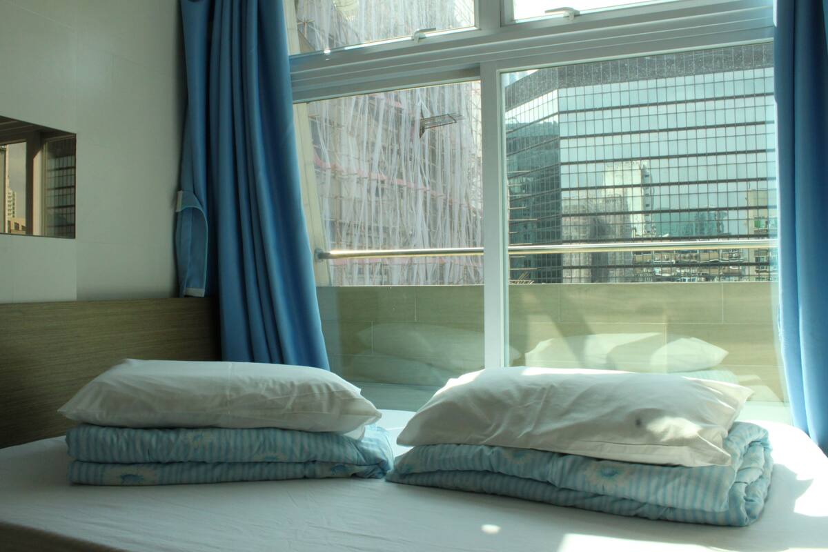 A hotel room with a bed, blue curtains, and a window with a view of buildings.