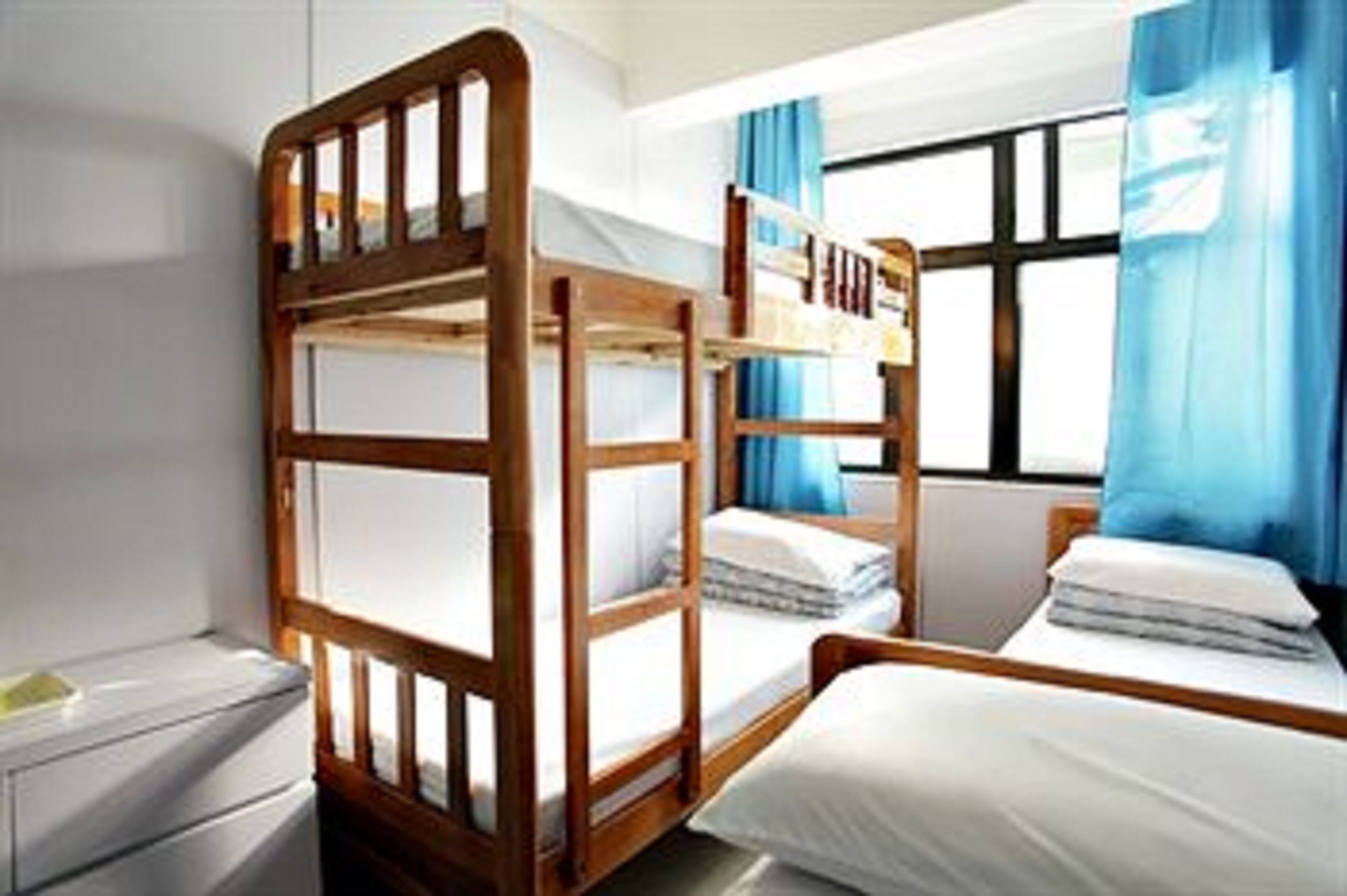 Een kamer met stapelbedden, een klein nachtkastje en een raam met gordijnen.