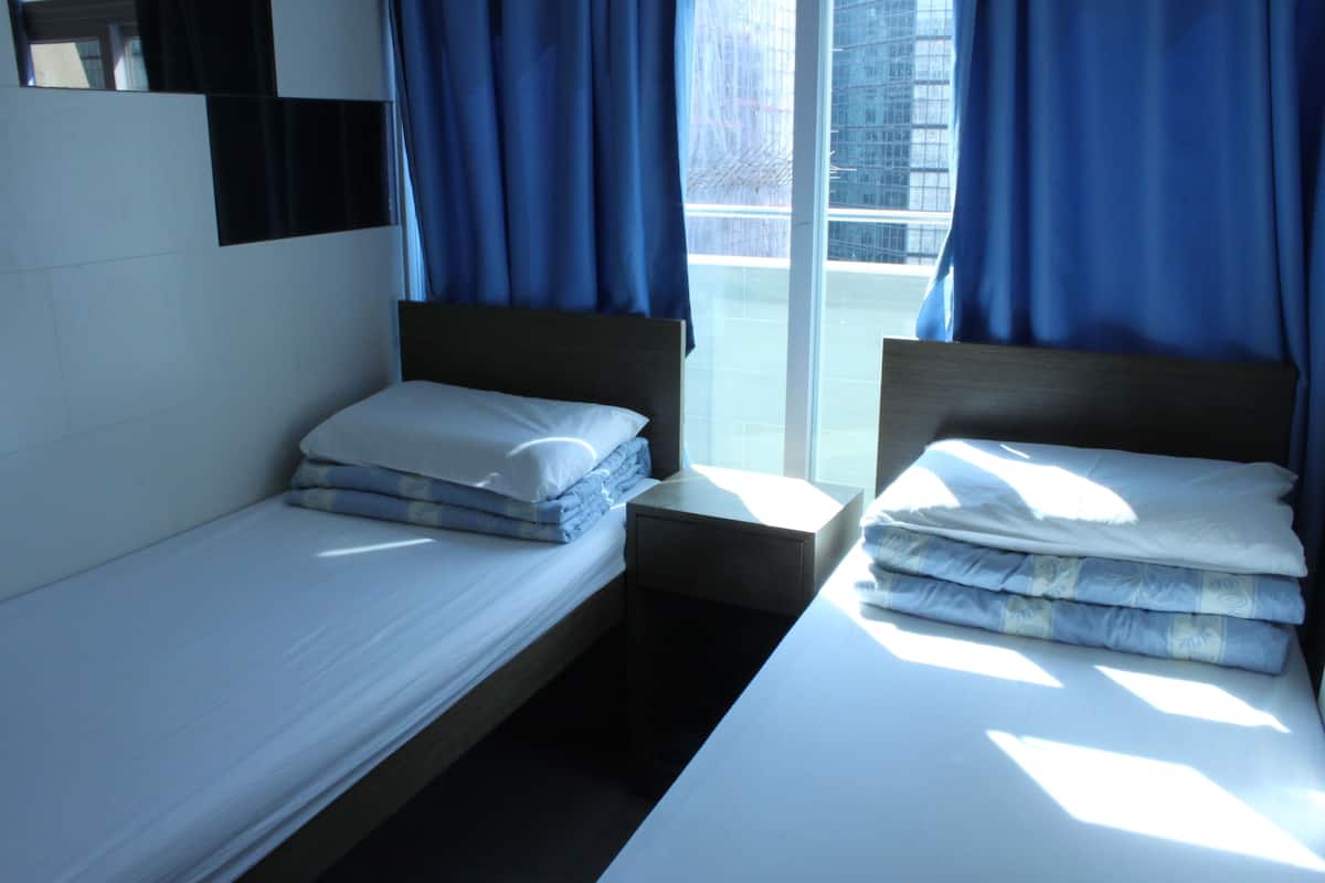 A hotel room with two single beds, a small bedside table, and a large window with curtains.