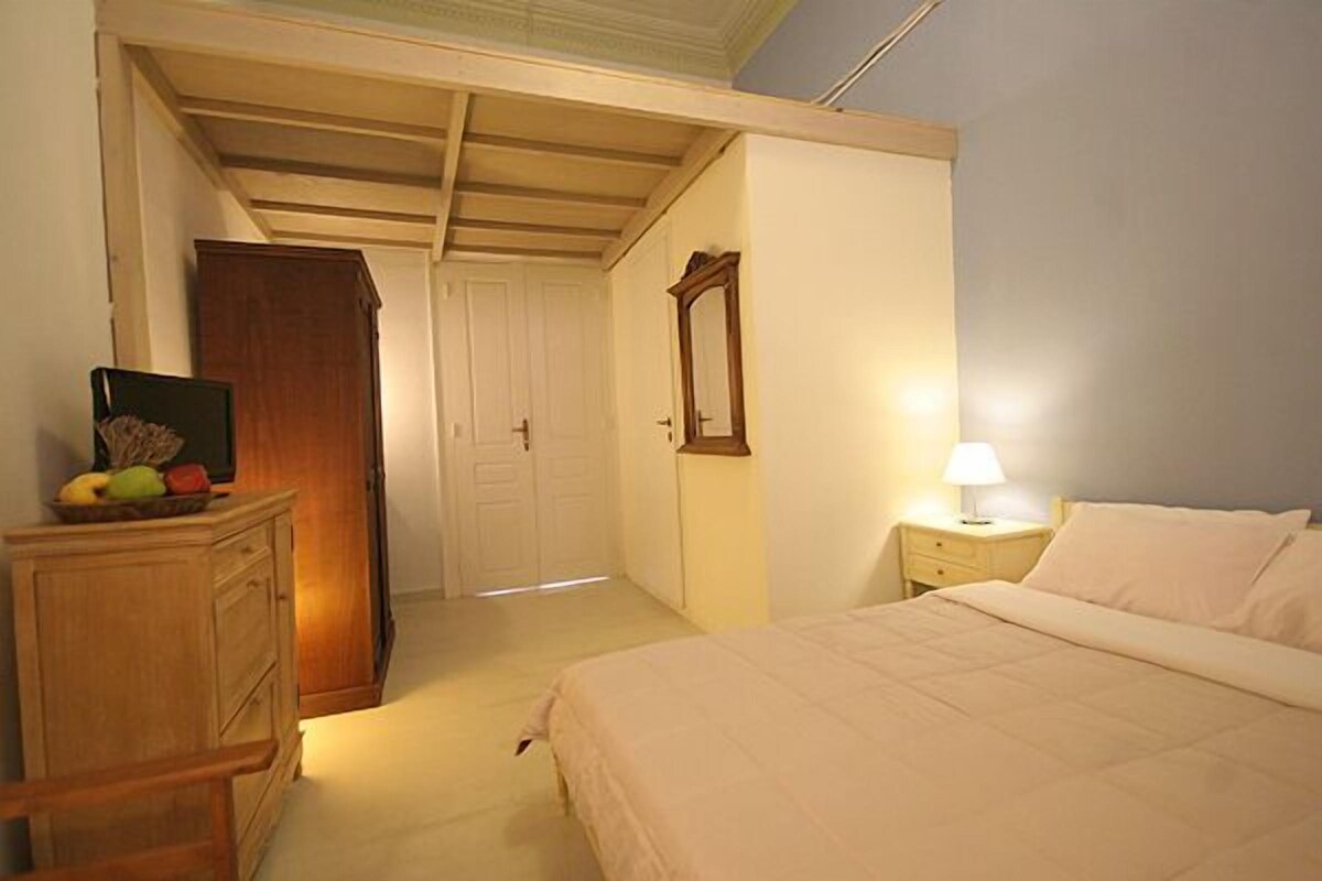 A bedroom with a bed, a nightstand, a dresser, a mirror, and a door.