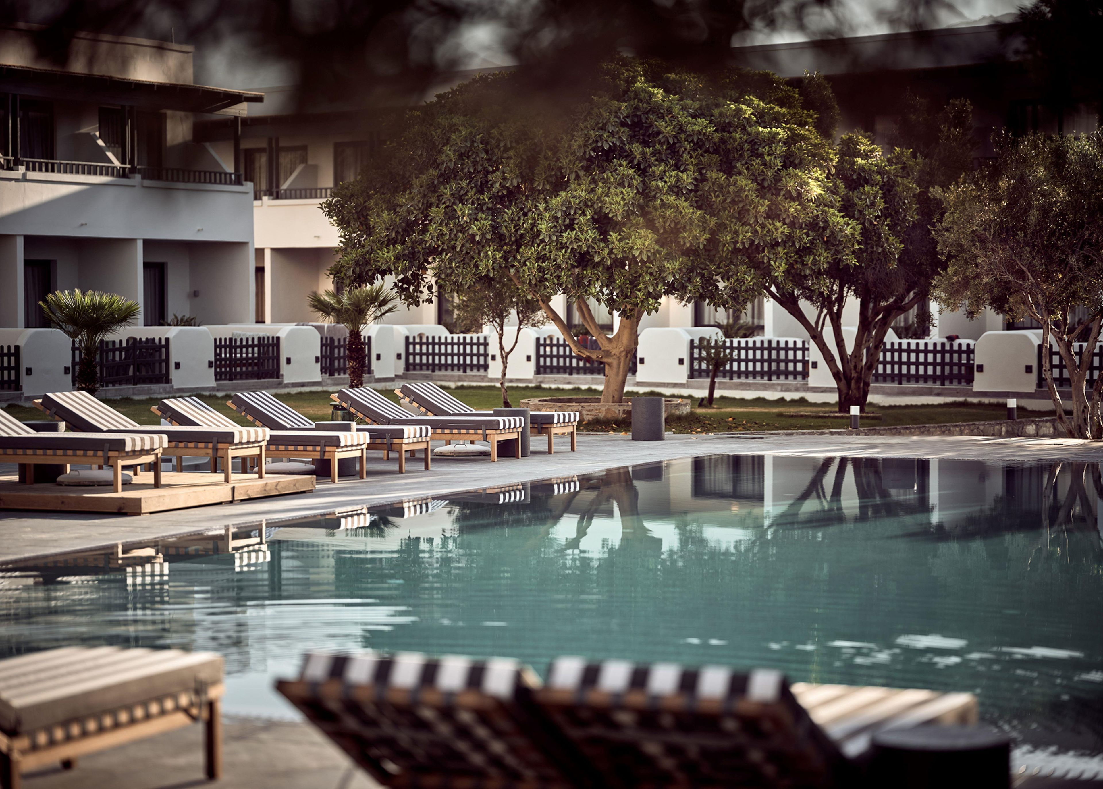Zona de piscina con sillas de descanso y un reflejo en el agua.