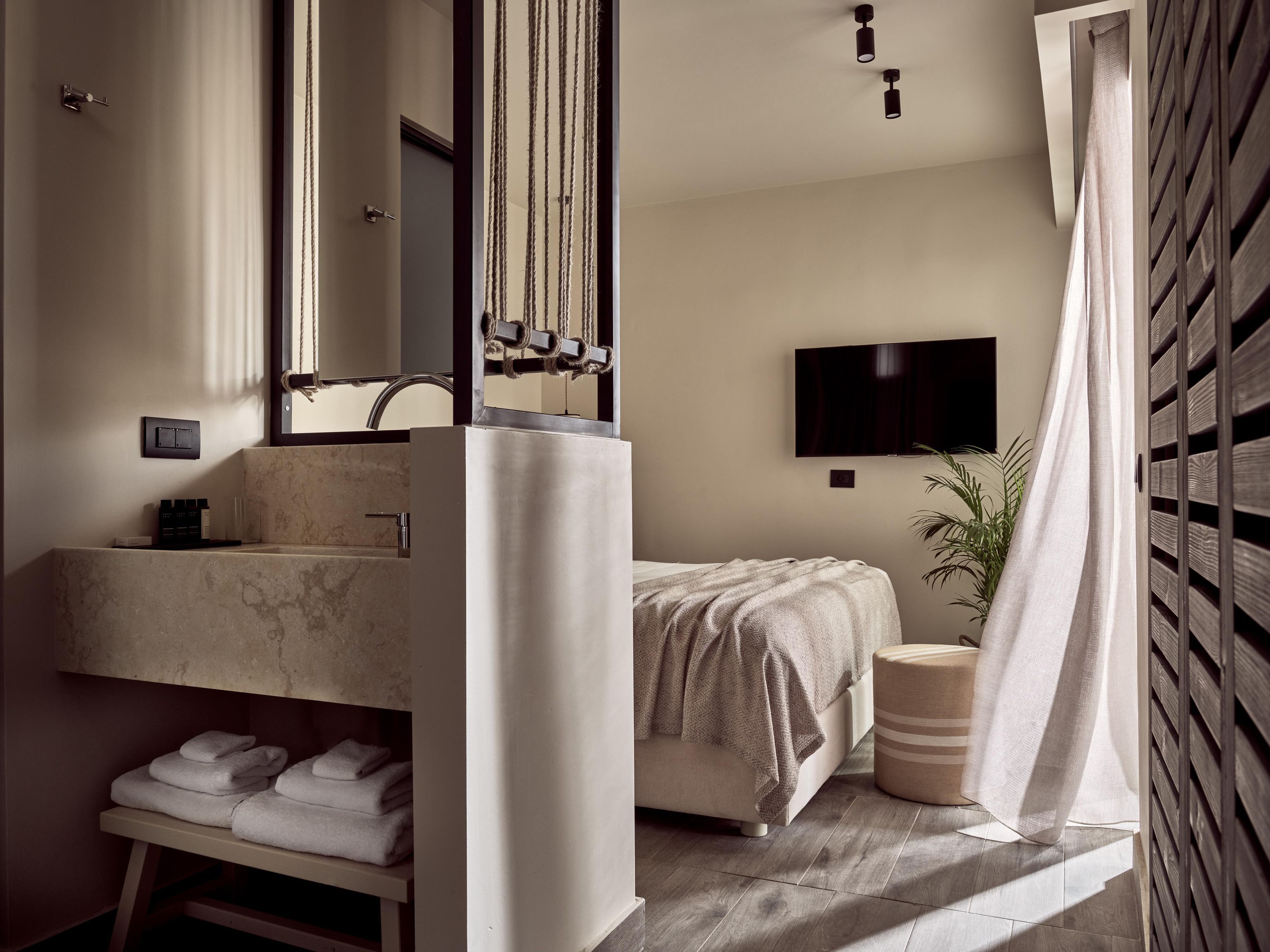 Casa de banho moderna com um espelho grande, lavatório e sanita. Há uma cama com um cobertor e uma planta em vaso.